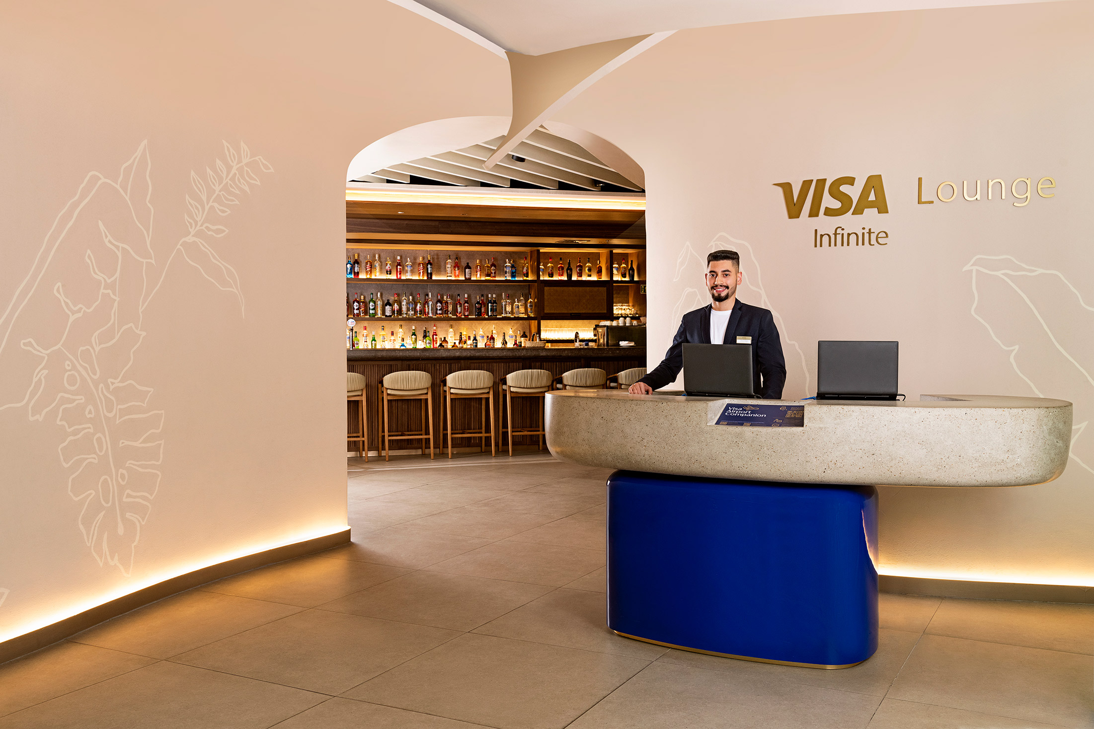 Recepção do Visa Infinite Lounge com recepcionista e bar ao fundo